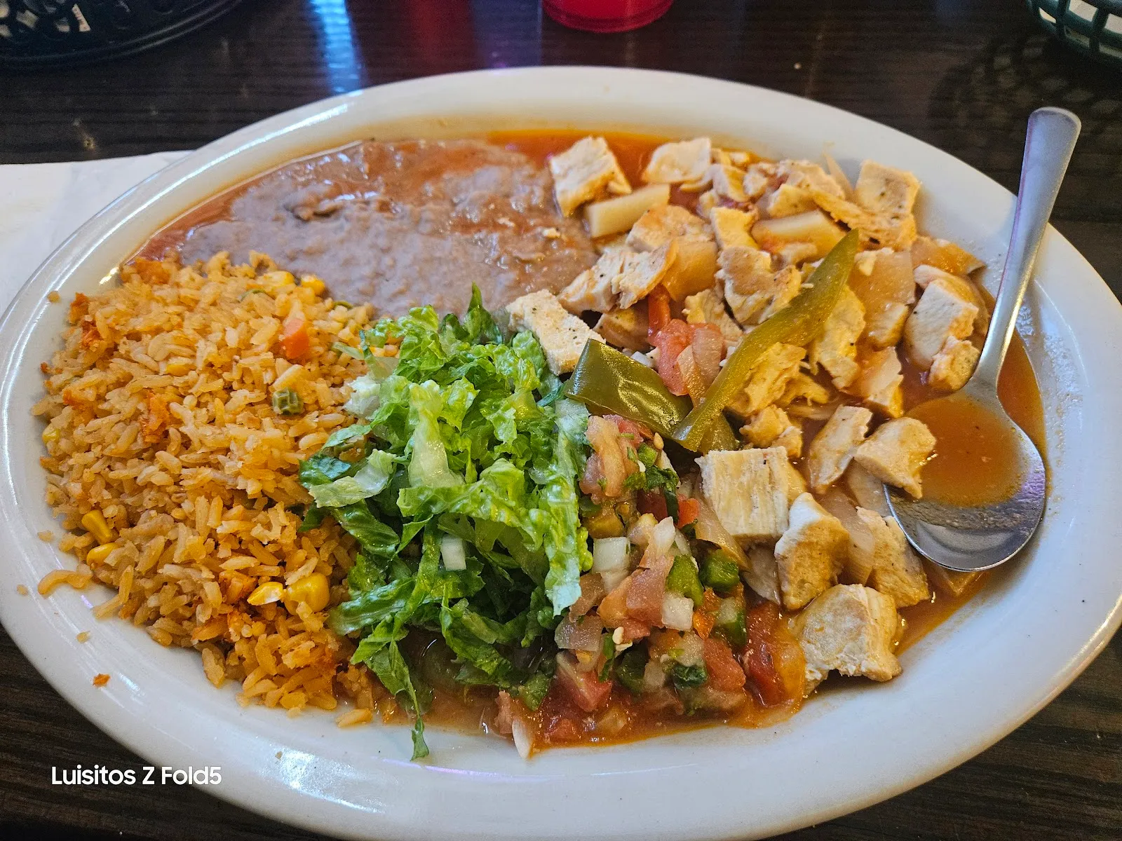 A grilled chicken plate with peppers in a savory broth, Mexican rice, refried beans, lettuce, and pico de gallo